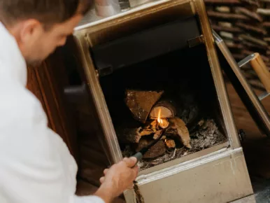 Homme allumant le poêle à bois du bain nordique au Lodge Miroir en Vendée