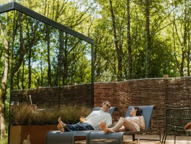 Couple sur les transats de la terrasse du Lodge Miroir face à la forêt, séjour insolite en Vendée